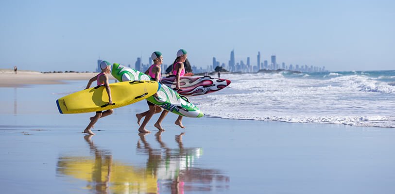 Three children walking on a beach, each carrying a surfboard under their arm