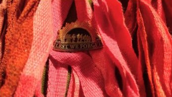 A bronze ANZAC badge pinned on a board of red canvas ribbons