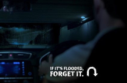 A person sitting in the driver seat of a car looking at a flooded road