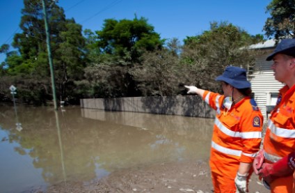 Two people dressed in State Emergency Service orange high visibility overalls and pointing at a flooded street