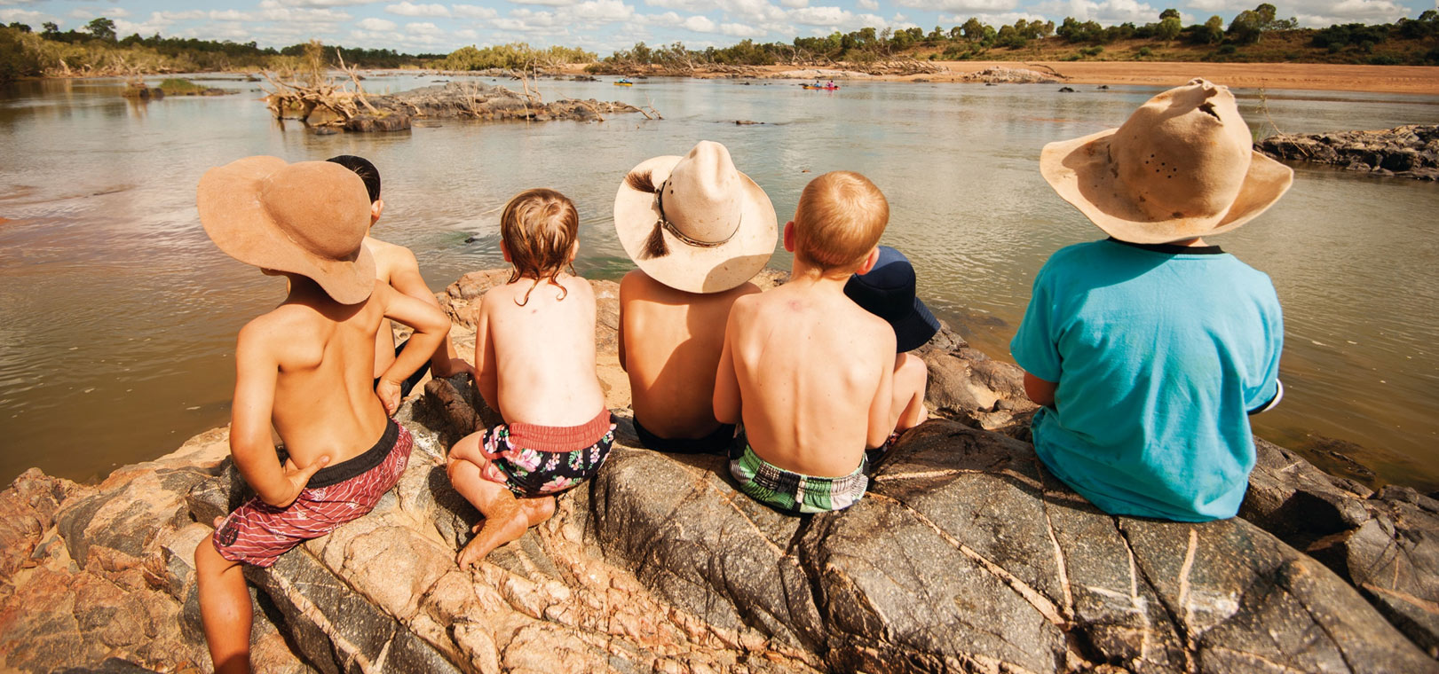 Group of kids in hats sitting on rocks near water